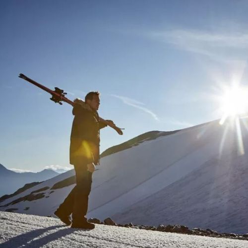 ein mann mit warmem parka und skis geht auf skitour